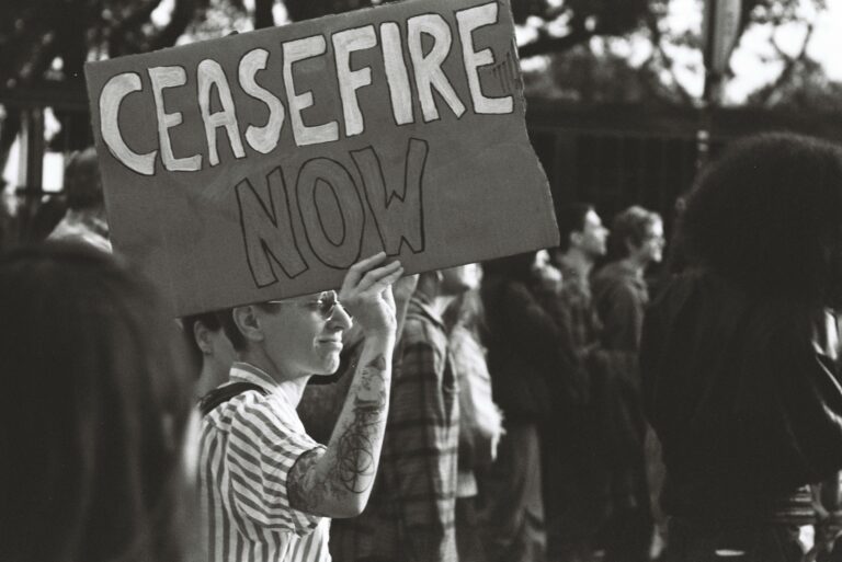 Black and white photo of a protest in Lisbon with a person holding a 'Ceasefire Now' sign.