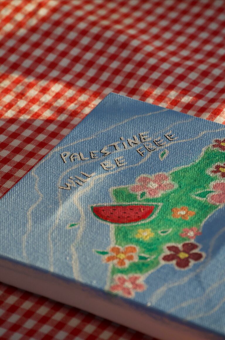 Close-up of a handmade canvas on a red checkered tablecloth, featuring a colorful map and flowers.