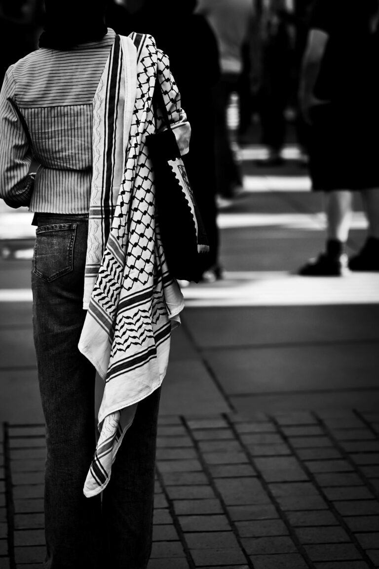 A monochrome image of a person wearing a keffiyeh at a street protest, symbolizing solidarity.