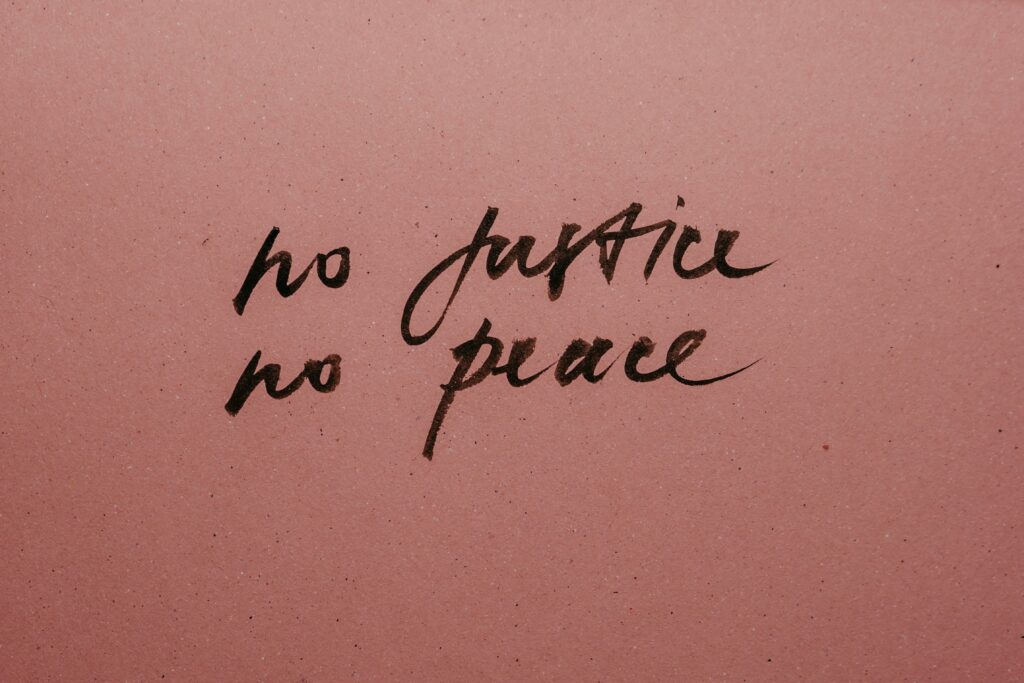 Handwritten ink slogan 'No Justice No Peace' on a pink background promoting social justice.
